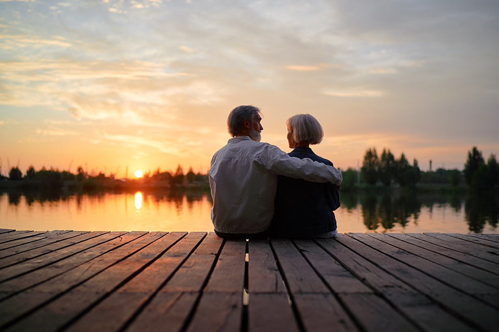 retired couple sitting on dock at sunset
